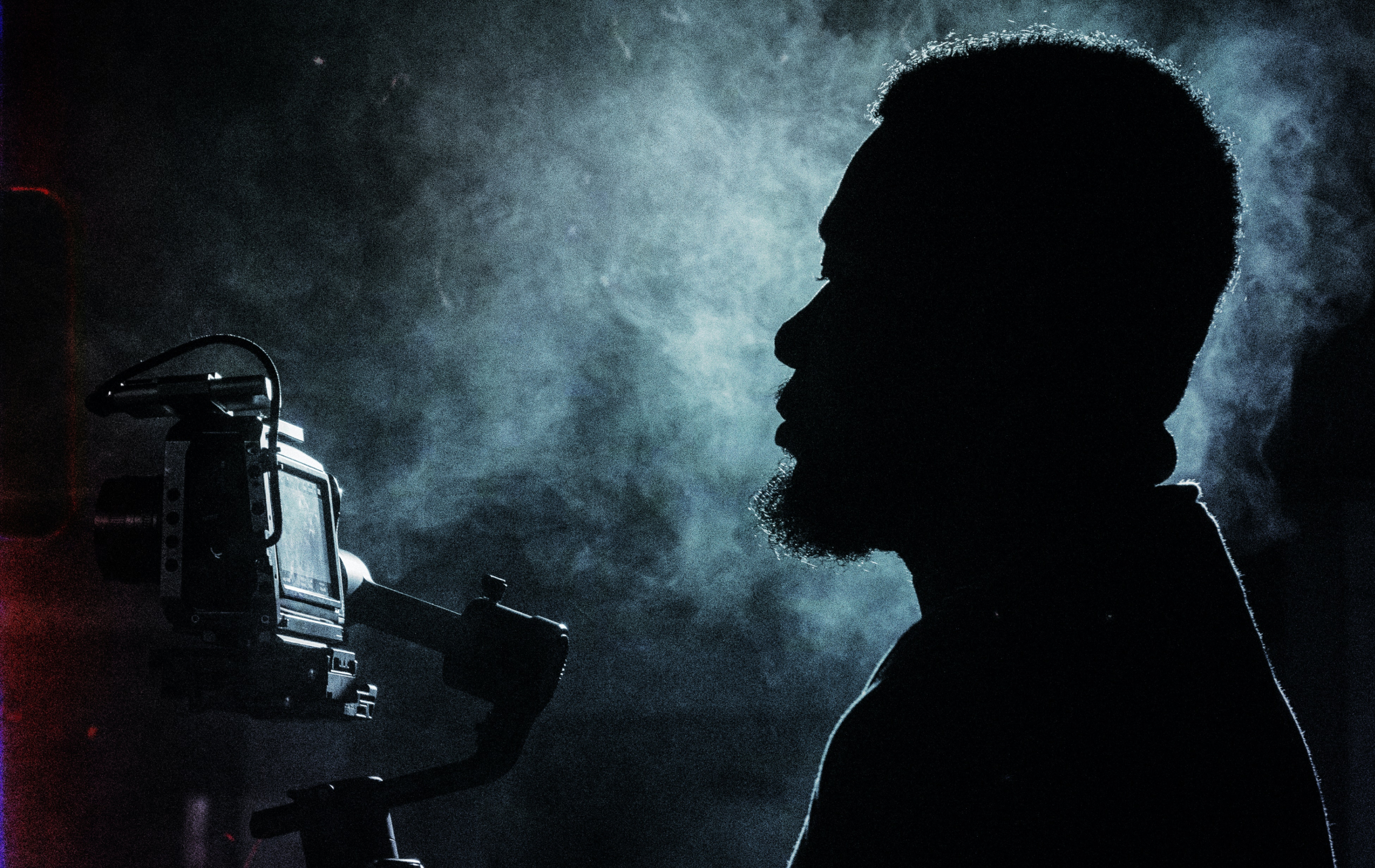A profile, silhouetted photo of a black videographer with a camera  